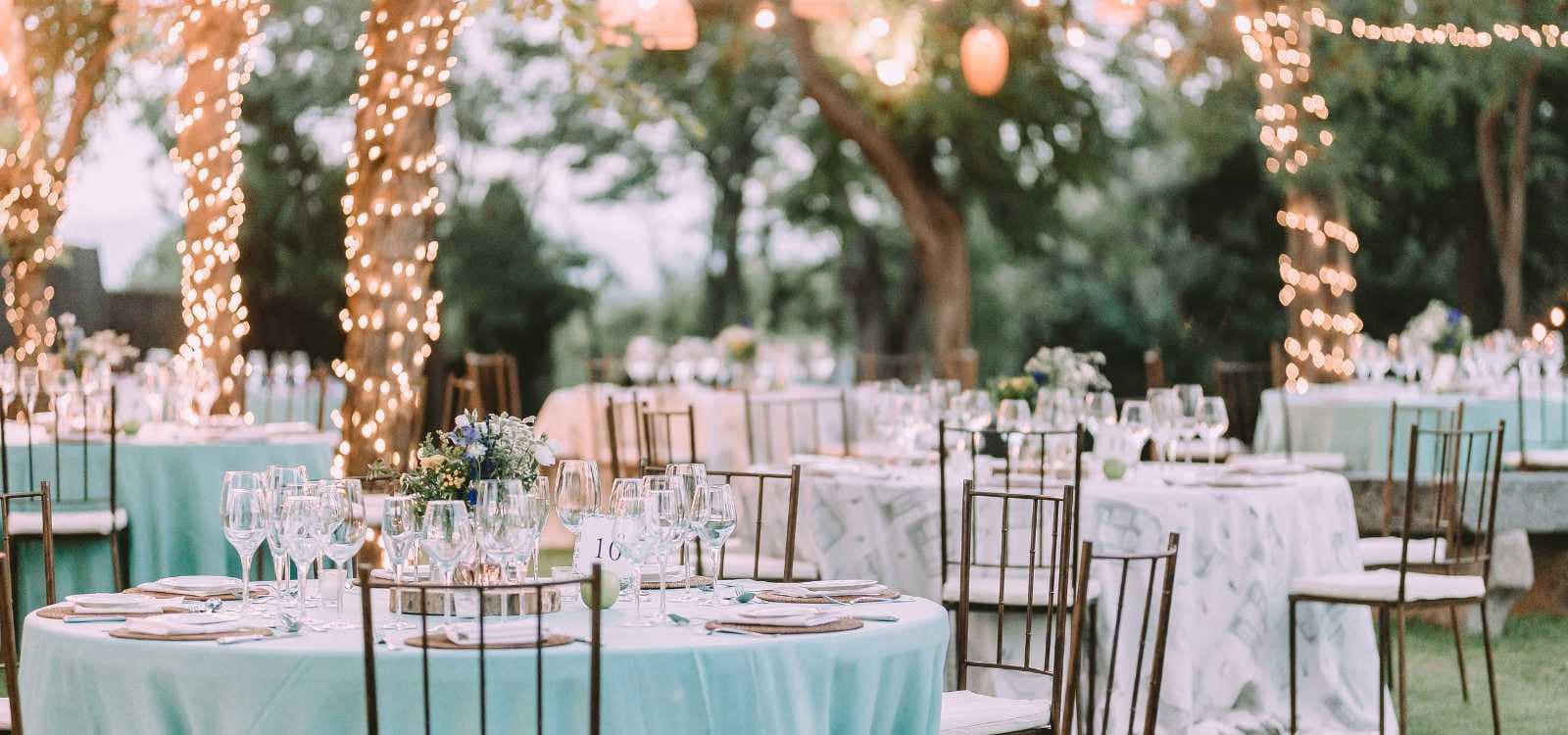 Gedeckte Tische mit Lichterketten bei einer Gartenhochzeit